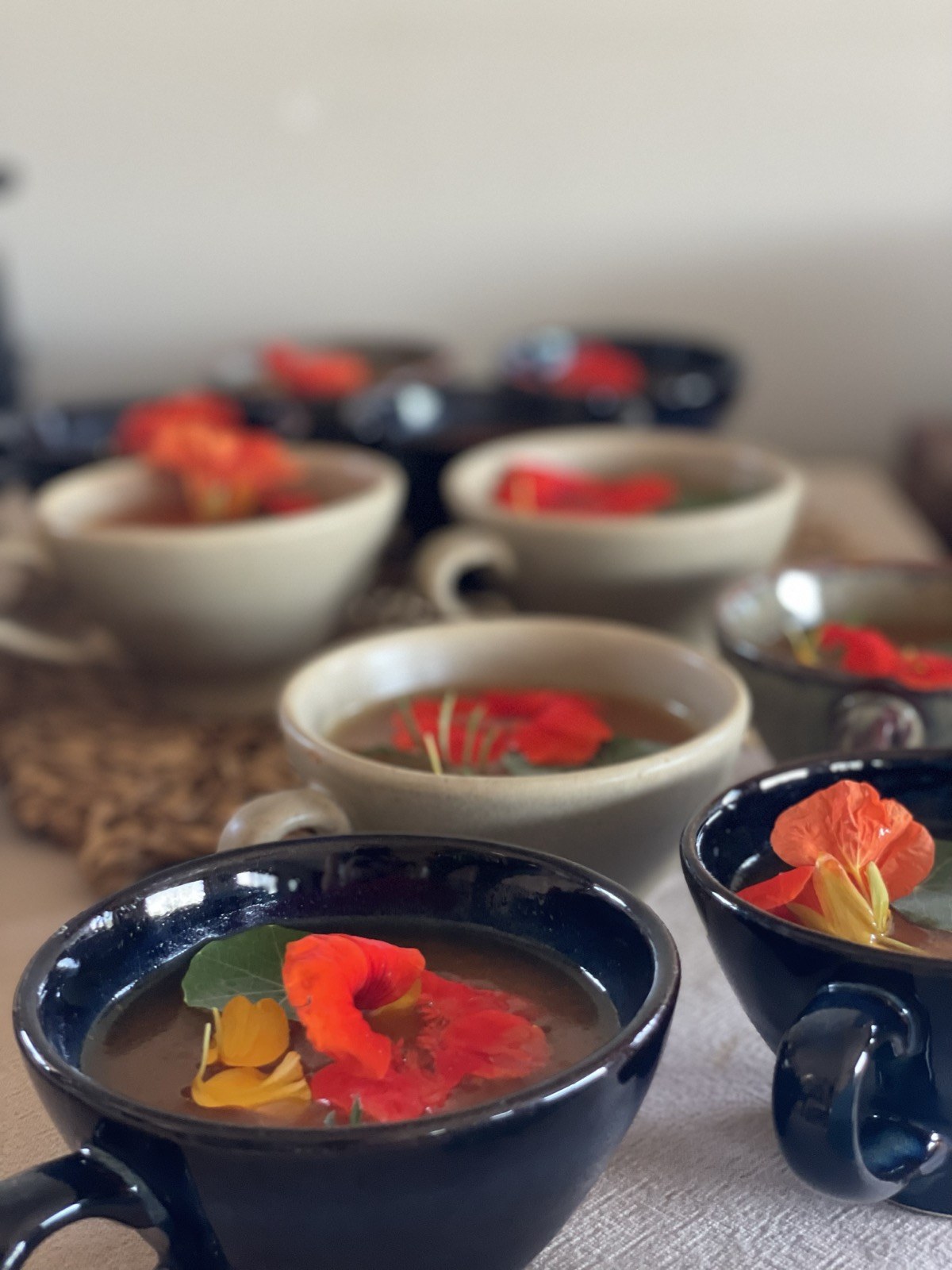 Handmade stoneware cups of clear broth crowned with nasturtium flowers