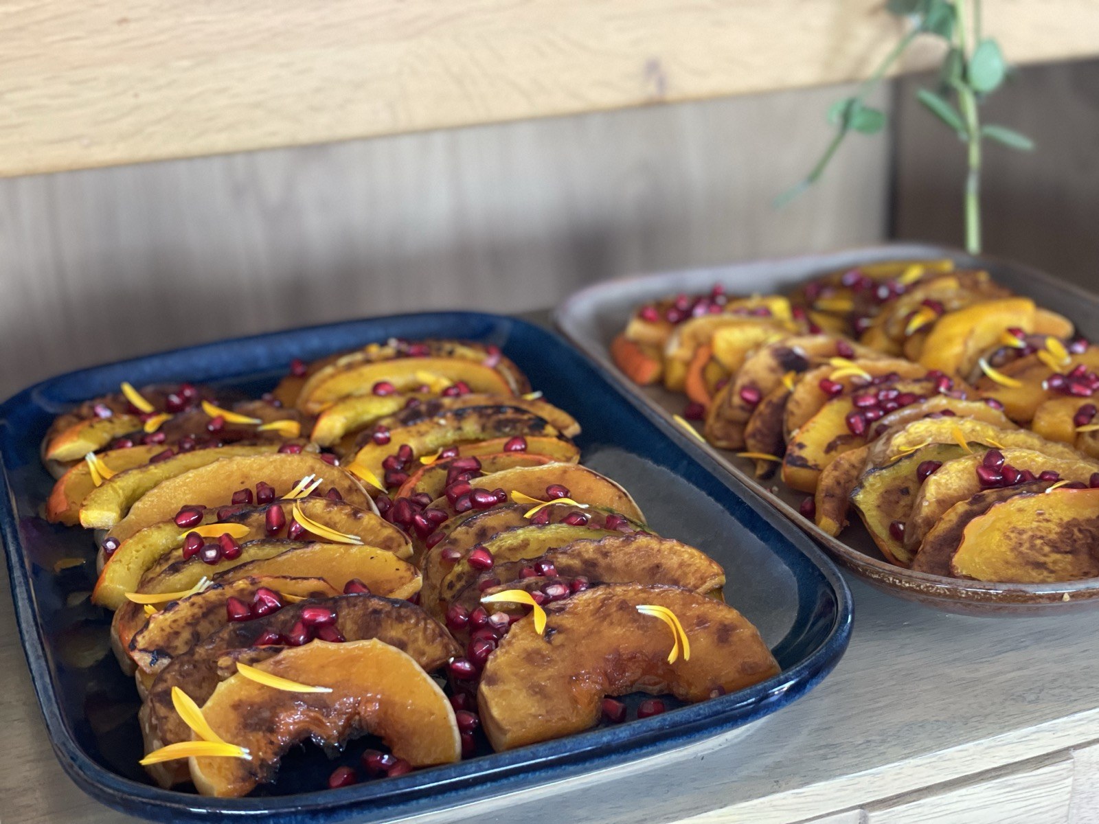 Glazed roasted pumpkin wedges with pomegranate and calendula petals on a cobalt ceramic platter